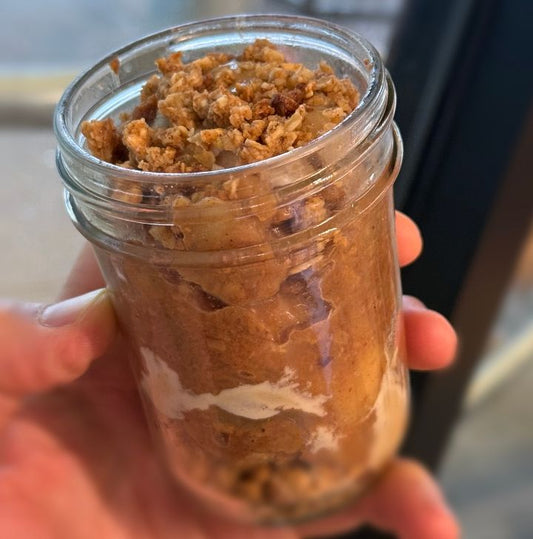 A jar filled with layers of apple, oats, and other ingredients, resembling a prepared dessert.