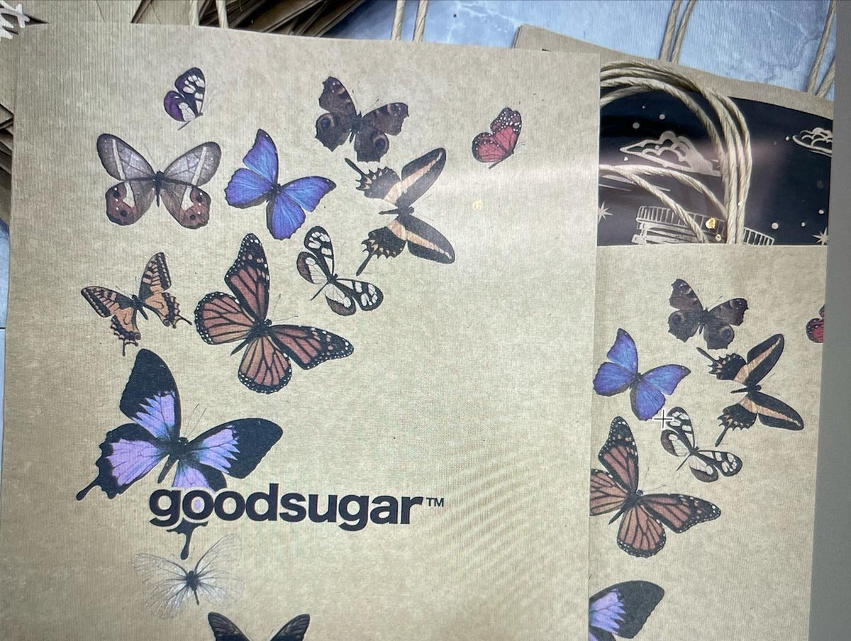 During construction, sample test-prints of shopping bags came in. Made from kraft paper, printed with colorful butterfly illustrations and the 'goodsugar' logo, shown against a neutral background.
